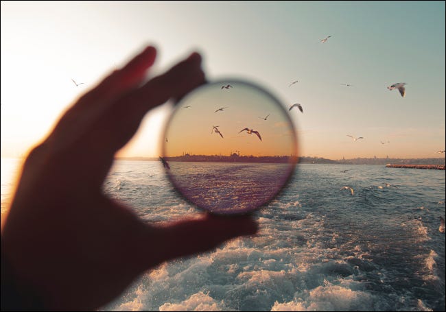 Mano sosteniendo un filtro de lente para demostrar el efecto polarizador en una escena de playa.