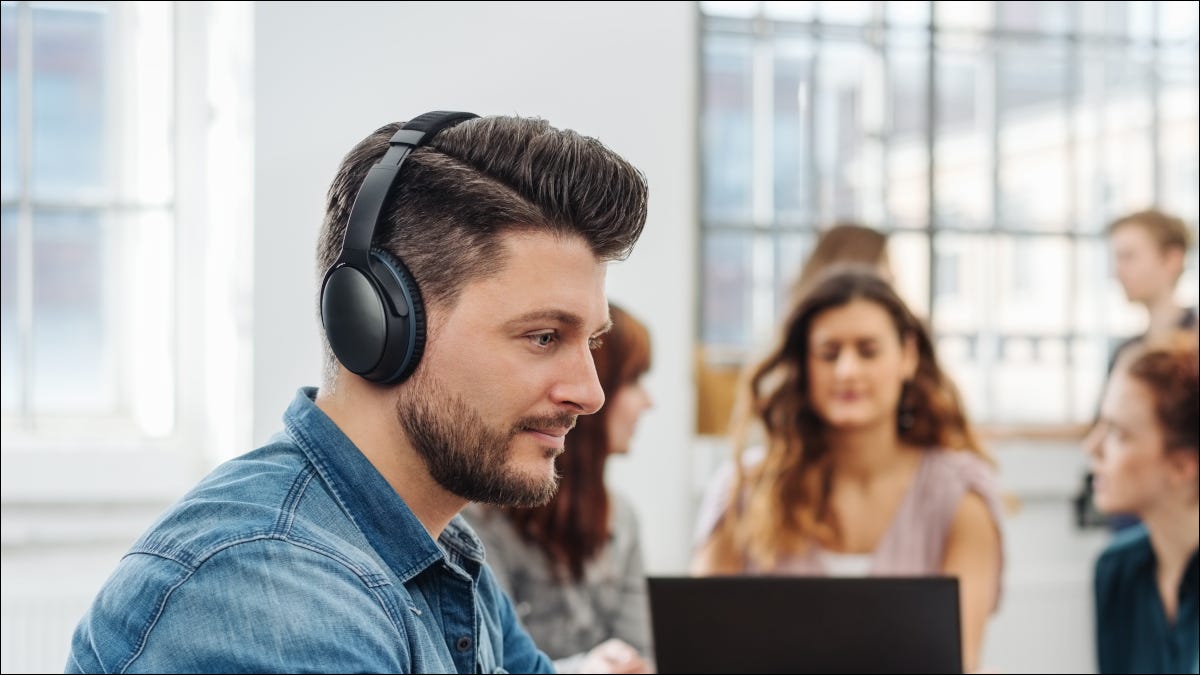 Hombre con auriculares en una oficina ocupada.