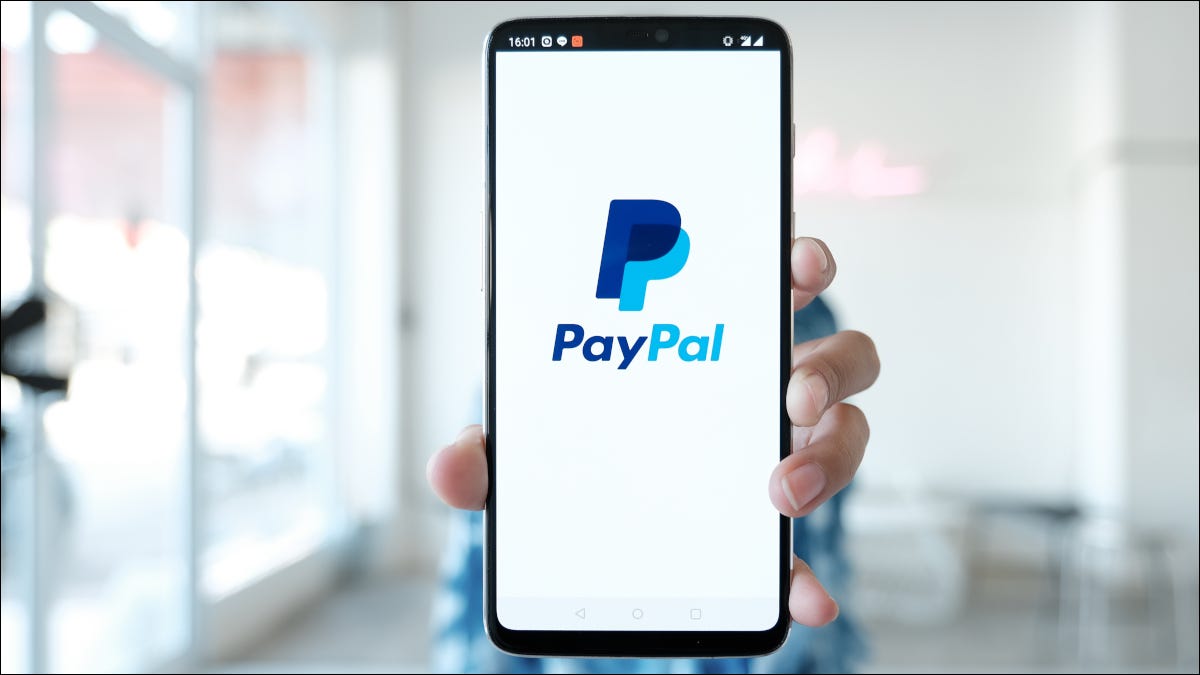Mano sosteniendo un teléfono inteligente con el logotipo de la aplicación de PayPal en la pantalla.