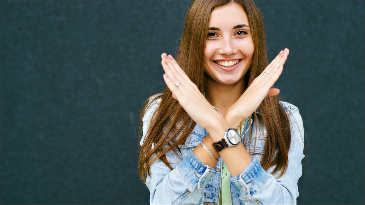 Mujer joven sonriendo y cruzando los brazos para formar una "X".