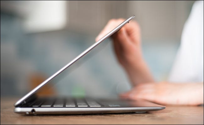 Una persona cerrando o abriendo la tapa de una computadora portátil