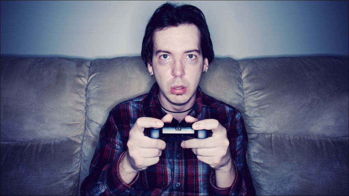 Hombre sentado en un sofá y jugando videojuegos con una expresión exhausta o aturdida.