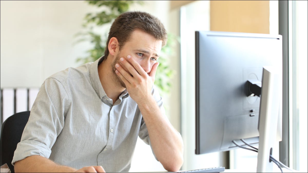 Hombre mirando la computadora con expresión de asombro, cubriendo la boca.