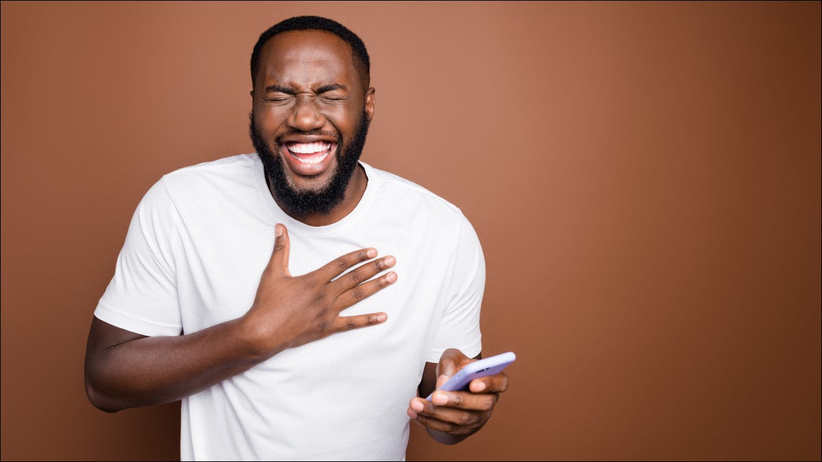 Hombre riendo mientras sostiene un teléfono inteligente.