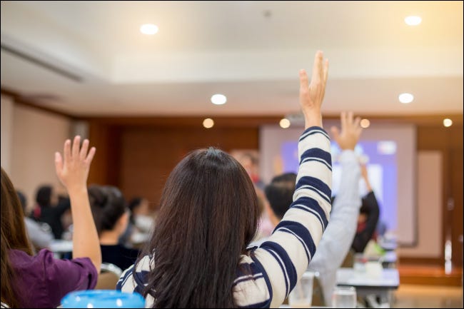 Gente de negocios levantando la mano para hacer preguntas en una conferencia.