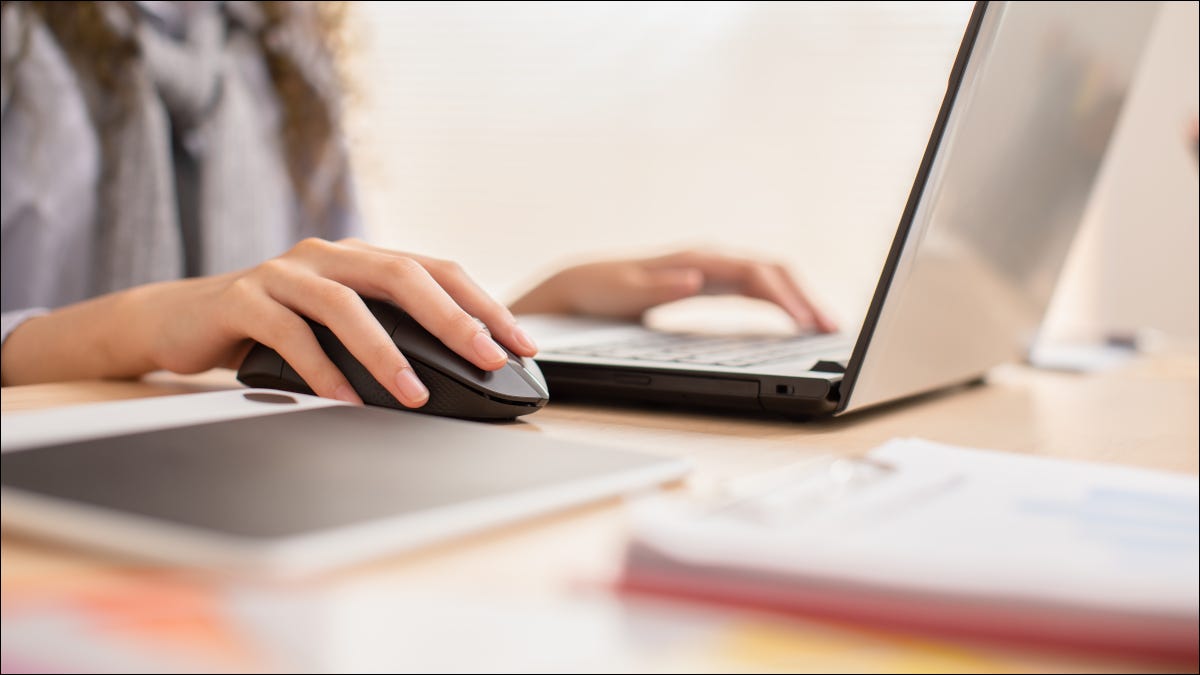 Una mujer que usa un mouse inalámbrico con su computadora portátil.