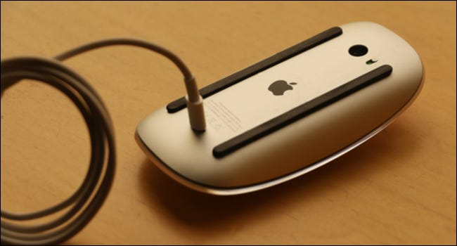 Un mouse Apple al revés con el cable de carga conectado.