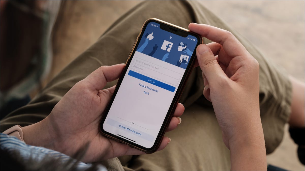 Persona que sostiene un iPhone con la pantalla de inicio de sesión de la aplicación de Facebook visible.