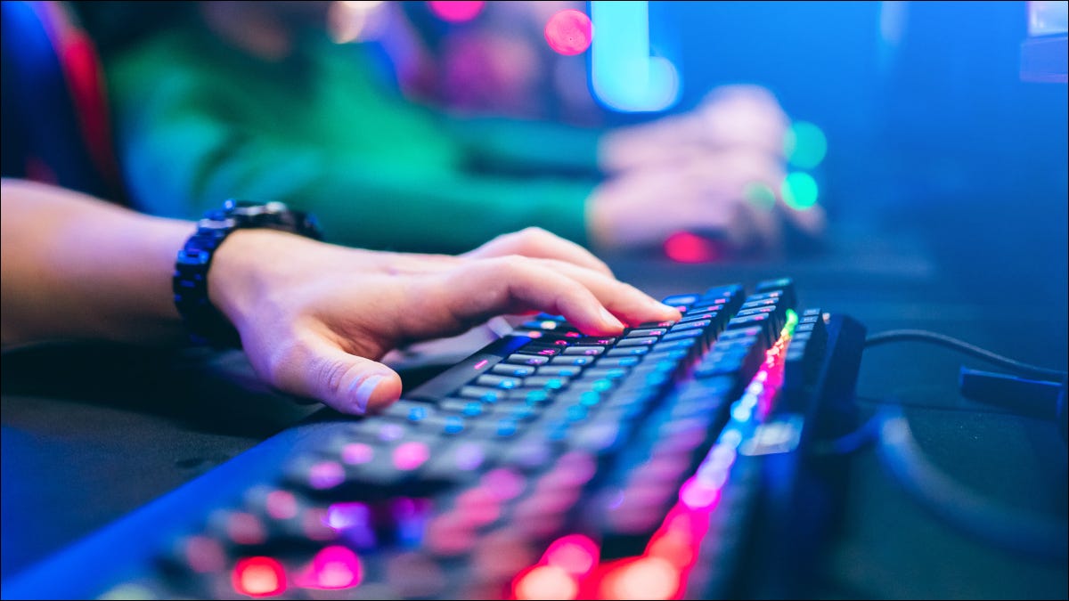 Primer plano de la mano de una persona en un teclado con iluminación RGB.