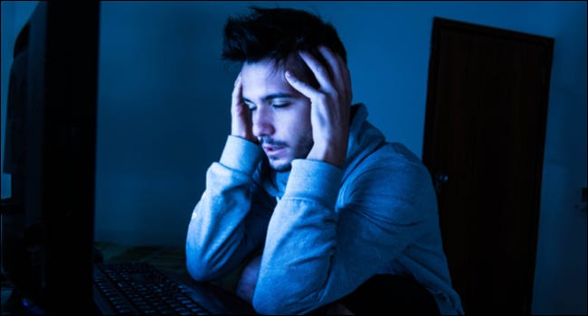 Hombre que parece estresado o agotado mientras usa una computadora en la oscuridad.