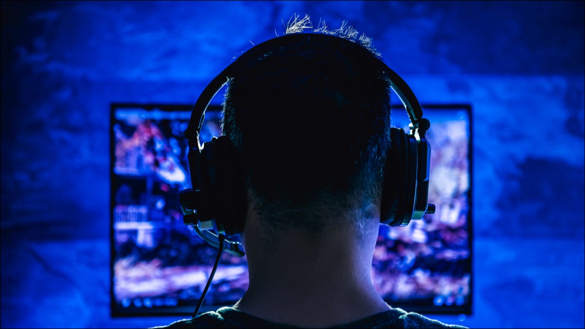 Parte posterior de la cabeza de un hombre mientras juega a altas horas de la noche con auriculares con cable puestos.
