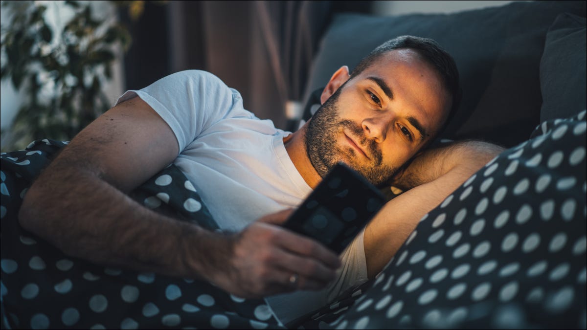 Hombre usando un teléfono inteligente mientras está acostado en la cama.