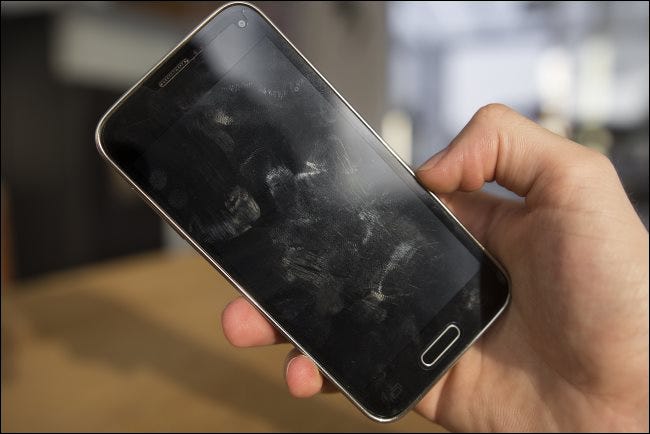 Una mano que sostiene un teléfono Android con manchas en la pantalla.