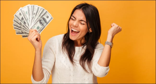 Una mujer con una expresión emocionada sosteniendo un abanico de billetes de cien dólares.