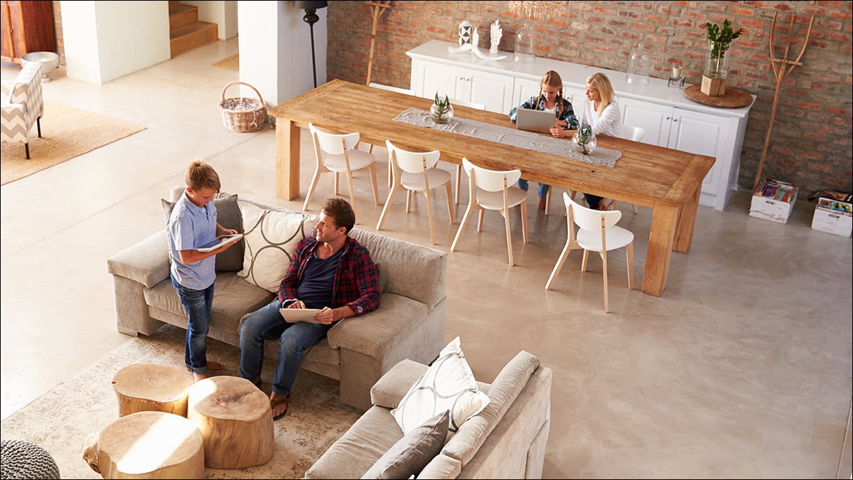 Una familia que usa tabletas y computadoras portátiles en un espacioso espacio habitable de concepto abierto.