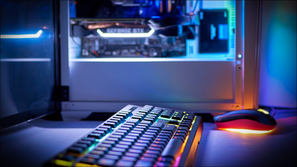 Teclado con iluminación RGB con una torre de PC iluminada en el fondo.