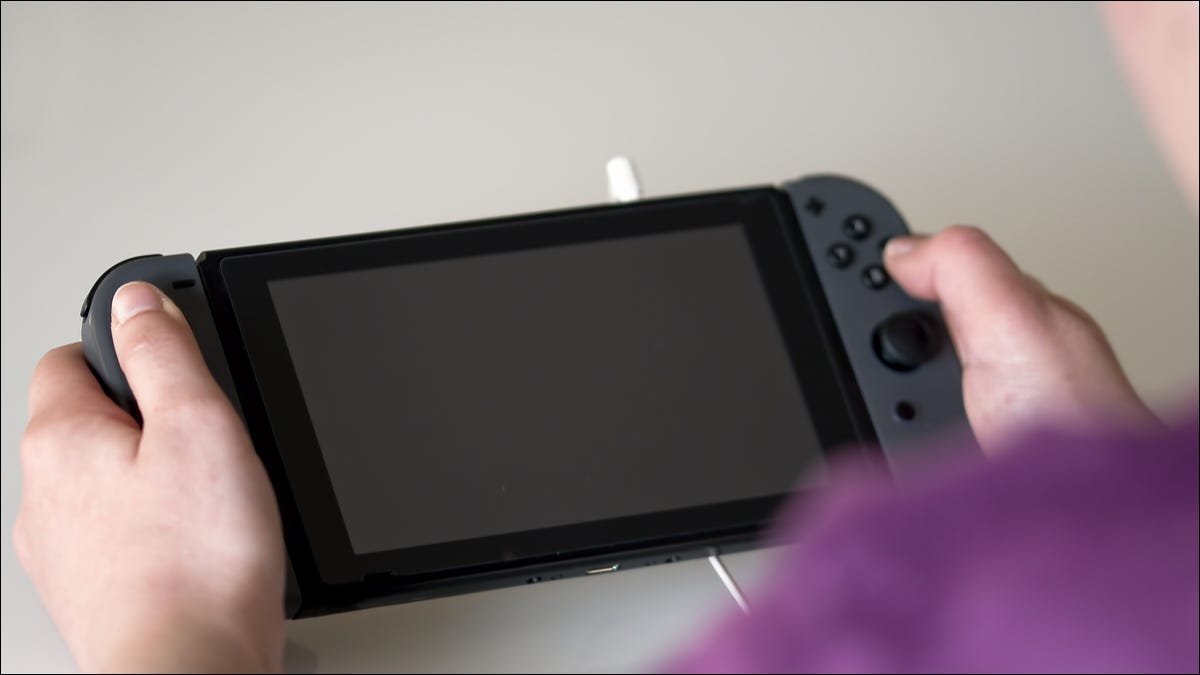 Persona presionando botones en un Nintendo Switch con la pantalla apagada.