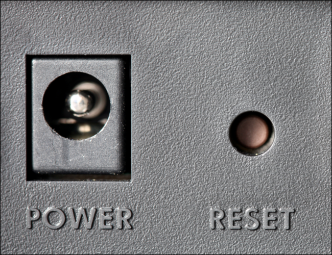 Un botón de reinicio insertado junto a un conector de alimentación.