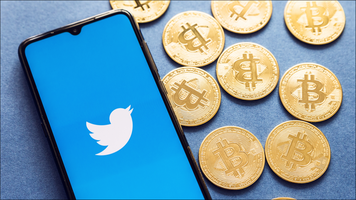 La aplicación de Twitter en un teléfono inteligente con monedas Bitcoin al lado.