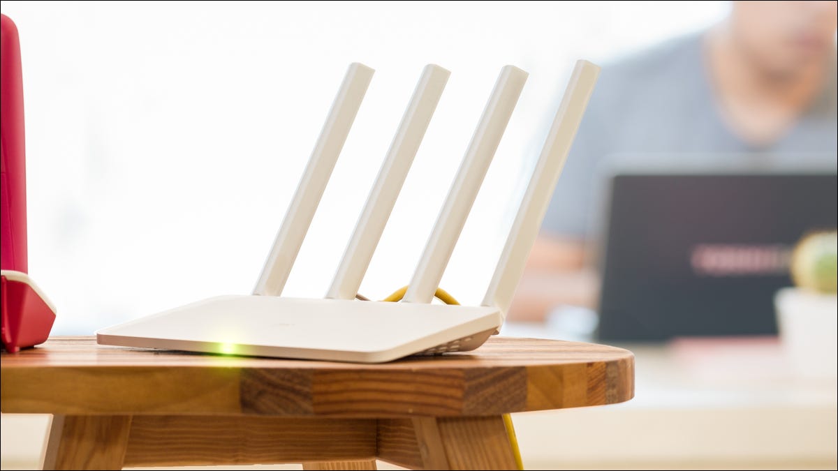 Enrutador Wi-Fi blanco sobre una mesa con un hombre usando una computadora portátil en el fondo.