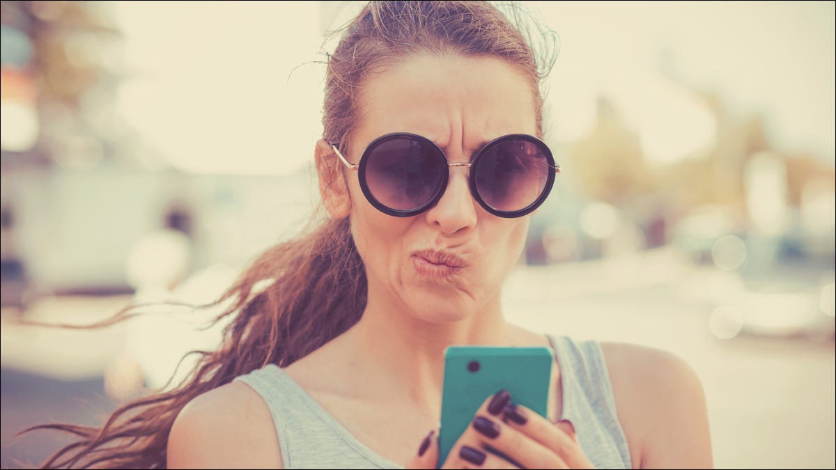 Mujer mirando su teléfono inteligente con una expresión disgustada o escéptica.