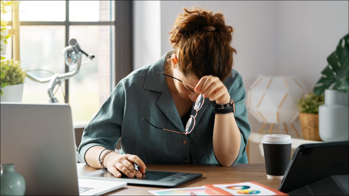 Mujer en una oficina con dolor de cabeza mientras usa tecnología.